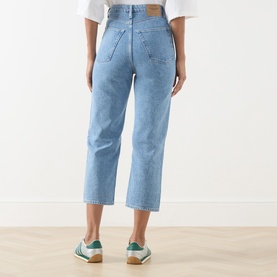 Model wearing American Vintage Joybird Cropped Straight-Leg Jeans in Authentique Stone, light wash denim, rear view, styled with white top and green