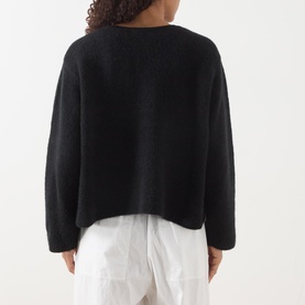 Model wearing American Vintage Vitow Knitted Sweater in black, showing rear view with boat neck and ribbed trims, styled with white trousers.
