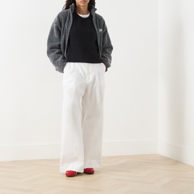 Model wearing American Vintage Vitow Knitted Sweater in black with grey fleece jacket, white wide-leg trousers and red flats.