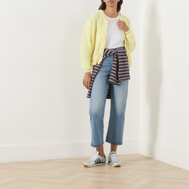 Model wearing American Vintage knitwear in citronnier chine yellow, styled with white tee, blue straight-leg jeans, striped shirt tied at waist, and