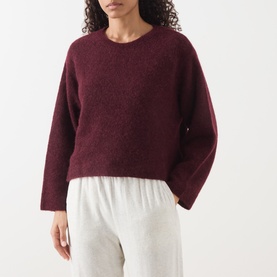 Model wearing American Vintage Vitow Knitted Sweater in Grenat Chine, crew neck, dropped shoulders, styled with grey trousers.