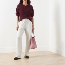 Model wearing American Vintage Vitow Knitted Sweater in Grenat Chine with cream wide-leg trousers, styled with a pink tote bag and burgundy loafers