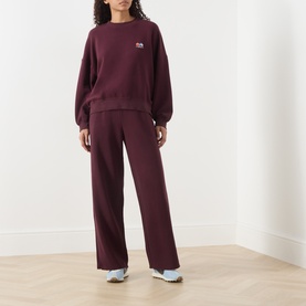 Model wearing American Vintage Atubay Drawstring Wide Leg Sweatpants in Lie de Vin, styled with matching sweatshirt and white trainers.