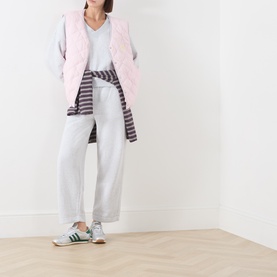 Model wearing American Vintage Gris Chine sweat bottoms, styled with a pink quilted gilet, grey V-neck tee, striped shirt and green trainers.