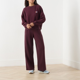 Model wearing American Vintage Atubay Logo Sweatshirt in lie de vin, styled with matching wide-leg trousers and blue trainers.