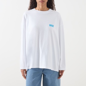 Model wearing American Vintage Gixy Logo Long-Sleeved Top in white with blue chest logo, crew neck, dropped shoulders, styled with blue jeans.