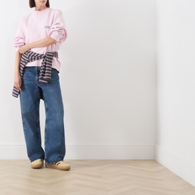 Model wearing American Vintage Sweat Top in Petale Vintage pink, styled with blue wide-leg jeans, plaid shirt tied at waist and beige loafers