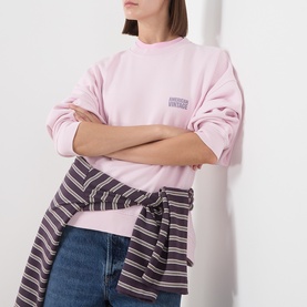 Model wearing American Vintage Sweat Top in Petale Vintage pink, arms crossed, styled with a striped shirt tied at the waist and blue jeans.