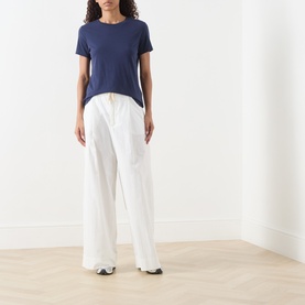 Model wearing American Vintage Apoly Solid T-Shirt in Night Star, crew neck, short sleeves, styled with wide-leg white trousers and black trainers.
