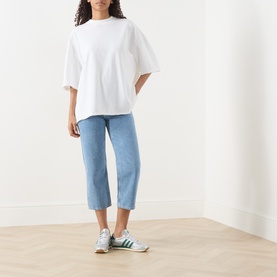 Model wearing American Vintage Afoma Oversized T-Shirt in white with round neck and rolled trims, styled with cropped blue jeans and green trainers.