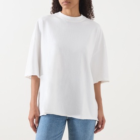 Model wearing American Vintage Afoma Oversized T-Shirt in white with mock neck, short sleeves and straight hem, styled with blue jeans.