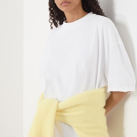 Model wearing American Vintage Afoma Oversized T-Shirt in white with round neck and rolled trims, styled with a yellow jumper tied at the waist.