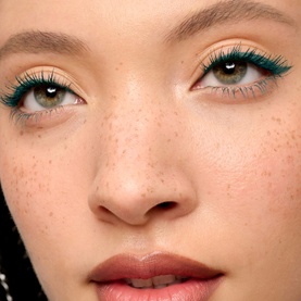 Model with Benefit Eye Liner in Rowdy Teal, shown as dramatic teal winged liner on upper lids with natural freckled skin and nude lips.
