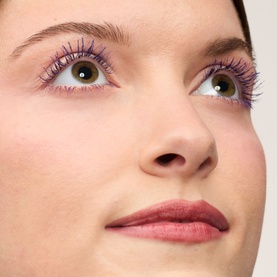 Model with Benefit mascara in Electric Purple, shown as bold violet lashes on upper and lower lashes, with a subtle pink lip