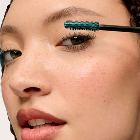 Model with Benefit mascara wand in Pumpd Up Teal applied to lashes, close-up showing teal-bristled applicator brush