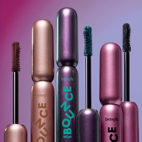 Benefit Badgal Bang mascara collection in Pumpd Up Teal, featuring multiple tubes with wands displayed against a purple-pink gradient background.