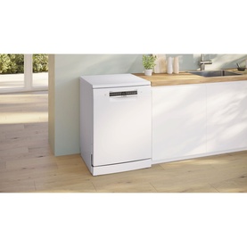 White freestanding dishwasher in a modern kitchen setting with light wood flooring and pale green cabinetry