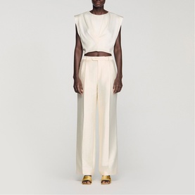 Model wearing Sandro clear cropped sleeveless top and wide-leg tailored trousers, styled with gold strappy heeled sandals.