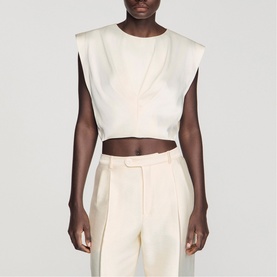 Model wearing Sandro cream sleeveless cropped top with shoulder pads, styled with matching wide-leg trousers