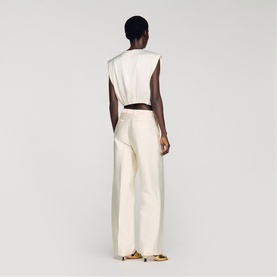 Model wearing Sandro clear wide-leg trousers, rear view, styled with a matching sleeveless top and gold heels.