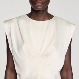 Model wearing Sandro sleeveless top in clear white with structured shoulders and front pleat detail