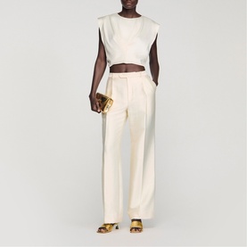 Model wearing Sandro clear wide-leg tailored trousers with cream sleeveless crop top, styled with gold strappy heels and clutch bag.