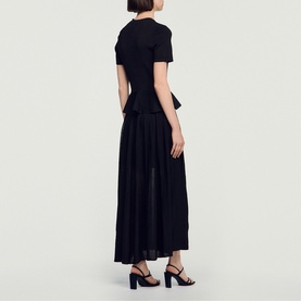Model wearing Sandro Peplum Flared Knitted Dress in black, maxi length with peplum waist and short sleeves, styled with black heeled sandals.