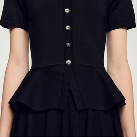 Model wearing Sandro Peplum Flared Knitted Dress in black, featuring silver button fastening and structured peplum waist detail.