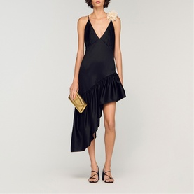 Model wearing Sandro black asymmetric ruffle hem dress with V-neckline, styled with black strappy heels and gold clutch bag.