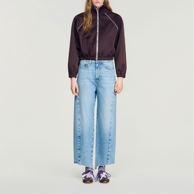 Model wearing Sandro brown zip-up cropped jacket with wide-leg light blue jeans and purple sandals