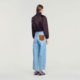 Model wearing Sandro brown zip-up top, styled with light blue wide-leg jeans featuring tan leather pocket detail, back view.
