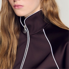 Model wearing Sandro Womens French Dress in brown, close-up of zip-up funnel neck with white contrast piping detail.