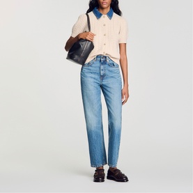 Model wearing Sandro cream short-sleeve knit top with blue collar, styled with light blue straight-leg jeans, carrying black tote bag