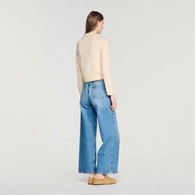 Model wearing Sandro cream cropped knit jumper, styled with wide-leg blue denim jeans, seen from behind.