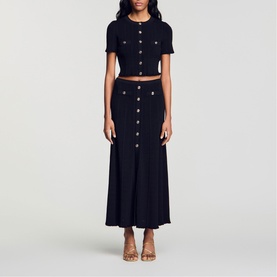 Model wearing Sandro Womens French Dress in black, featuring button-front crop top and midi skirt co-ord set, styled with tan heeled sandals.