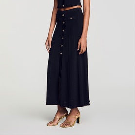 Model wearing Sandro black maxi skirt with front button detail, styled with a cropped top and gold heeled sandals