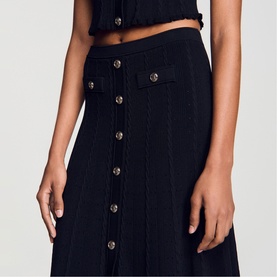 Model wearing Sandro black knit midi skirt with gold button-front detail, styled with matching black crop top