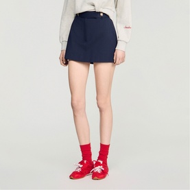 Model wearing Sandro navy blue mini skirt with gold-tone button detail, styled with red socks and red shoes