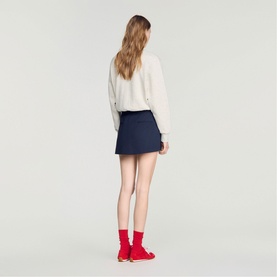 Model wearing Sandro Womens French Dress in navy blue mini skirt style, styled with cream sweatshirt and red socks with shoes, back view.