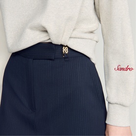 Model wearing Sandro Womens French Dress in navy blue ribbed fabric with gold logo buckle detail, styled with a grey marl sweatshirt.