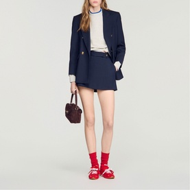 Model wearing Sandro navy blue blazer and matching shorts, styled with a white top, red socks, red shoes, and a burgundy handbag.