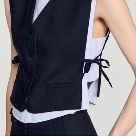 Model wearing a navy pinstripe tailored waistcoat with black ribbon tie detail at sides, styled over a white sleeveless blouse