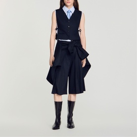 Model wearing navy sleeveless waistcoat and wide-leg culottes with bow detail, styled with light blue shirt and black knee-high boots