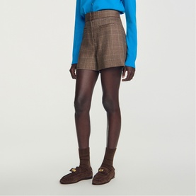 Model wearing Sandro brown checked high-waist shorts with blue top, styled with brown tights and gold-detail loafers.