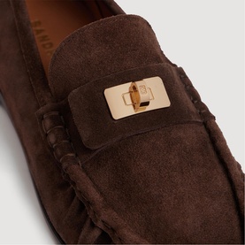 Sandro brown suede loafer with gold-tone twist-lock hardware detail and moccasin stitching, close-up view.