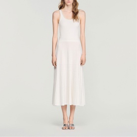 Model wearing Sandro Womens French Dress in clear, midi-length sleeveless style with pleated skirt, styled with strappy embellished sandals.
