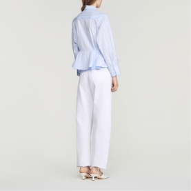 Model wearing Sandro sky blue striped cotton shirt with peplum hem and wide sleeves, styled with white wide-leg trousers and heeled mules
