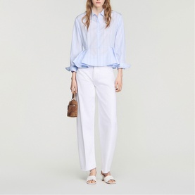 Model wearing Sandro sky blue striped oversized shirt with white wide-leg trousers, white sandals, and carrying a brown structured bag