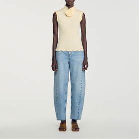 Model wearing cream sleeveless ribbed top with lettuce hem, styled with light blue barrel-leg jeans and tan sandals