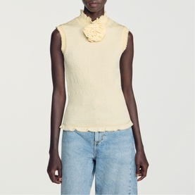 Model wearing pale yellow sleeveless knit top with corsage detail at neckline and lettuce hem, styled with blue jeans